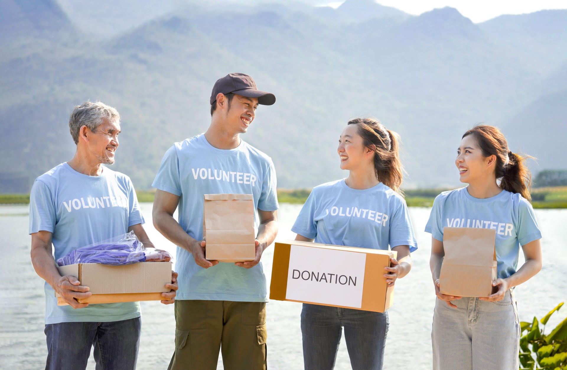 group of diverse people in unity wearing blue t-shirt holding donation box and donated items standing in the park or donation area