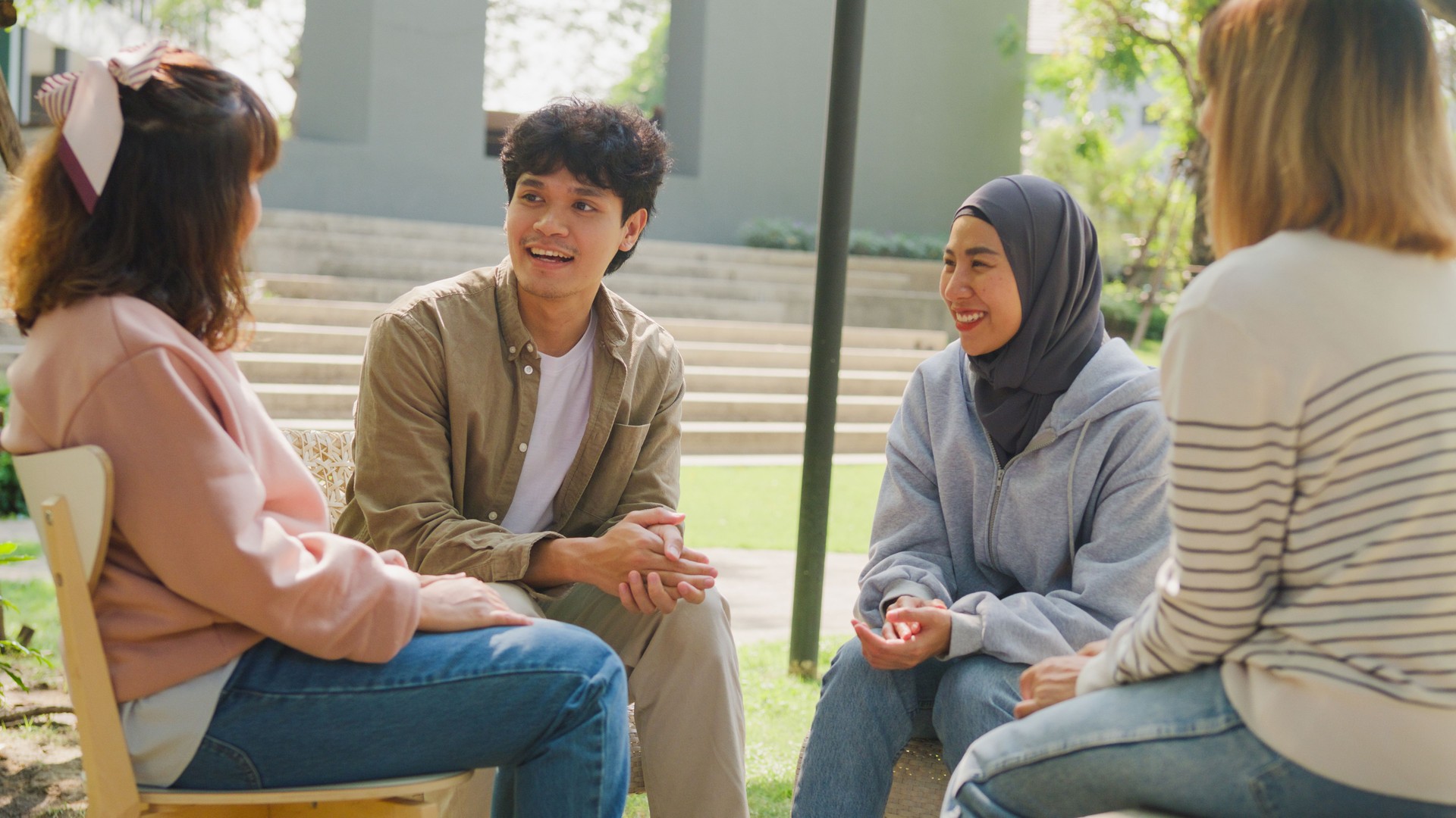 Small Asian group of people sit in a close circle and talk to a therapist in park. Smile people sharing story happy speak diverse people sitting in circle at group therapy session psychologist.